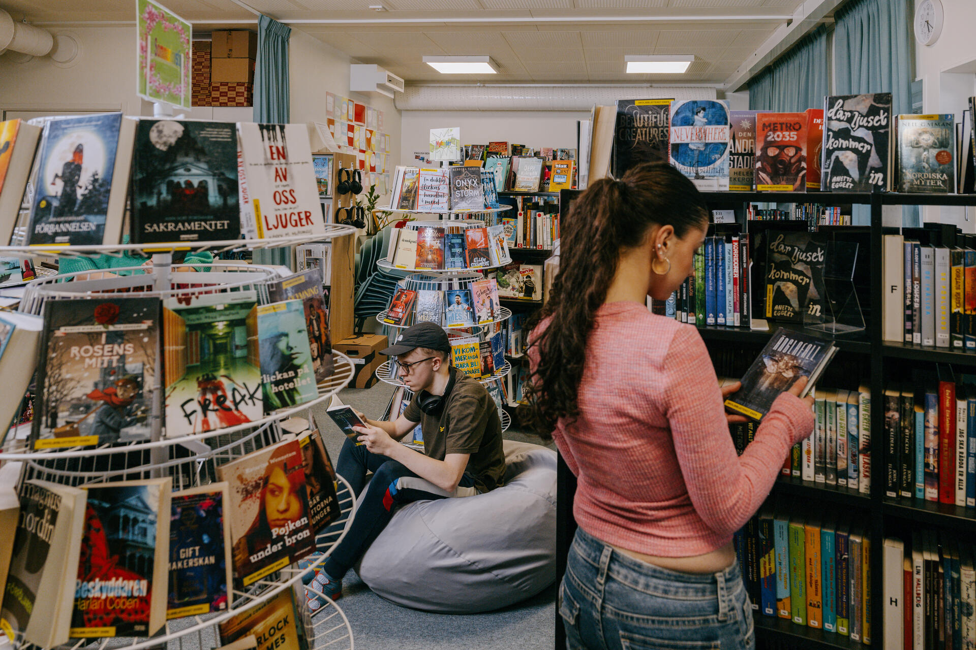 Elever vistas i skolbiblioteket i Expandias modullösning på Ekens skola i Hammarby Sjöstad, där de läser och väljer böcker bland bokhyllor i en lugn studiemiljö.