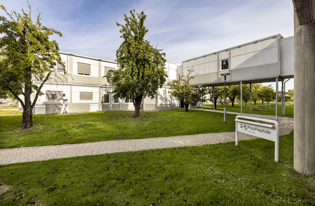 Kontorsmoduler hos Polypeptide placerade i grön utemiljö med gräsmattor, träd, gångvägar och uteplatser med picknickbord, samt tvåplansmoduler med fönsterrader – kontorsmoduler från Expandia.