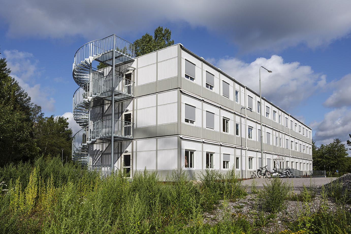 Tillfällig modulbyggnad från Expandia i tre våningar med kontorslokaler, placerad i grön stadsmiljö, med ljus fasad, många fönster och externa trappor.